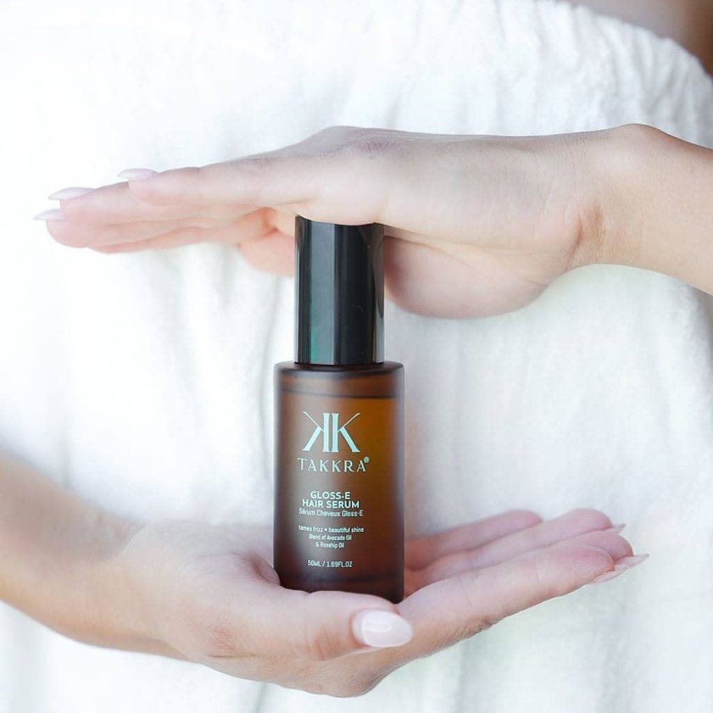 Woman holding a bottle of the Takkra Gloss-E Hair Serum